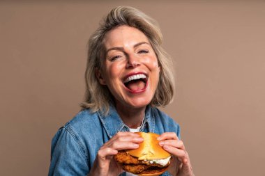 Renkli arka planda hamburger yiyen güzel olgun bir kadın elinde fast food sandviçi tutan orta yaşlı bir kadının portresi.