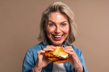 Renkli arka planda hamburger yiyen güzel olgun bir kadın elinde fast food sandviçi tutan orta yaşlı bir kadının portresi.