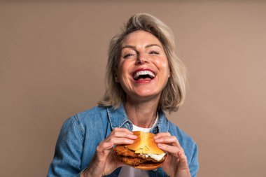 Renkli arka planda hamburger yiyen güzel olgun bir kadın elinde fast food sandviçi tutan orta yaşlı bir kadının portresi.
