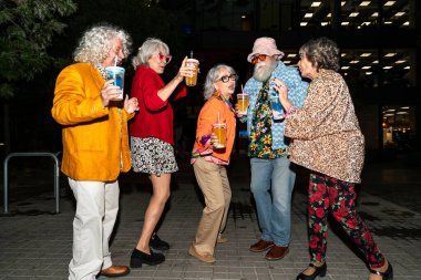 Süslü elbiseli mutlu son sınıf arkadaşları gecenin bir yarısı şehir sokaklarında parti veriyor. Şık kıyafetler giyen ve dışarıda eğlenen neşeli yaşlı insanlar.