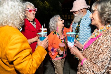 Süslü elbiseli mutlu son sınıf arkadaşları gecenin bir yarısı şehir sokaklarında parti veriyor. Şık kıyafetler giyen ve dışarıda eğlenen neşeli yaşlı insanlar.