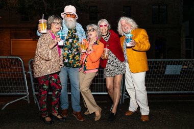 Süslü elbiseli mutlu son sınıf arkadaşları gecenin bir yarısı şehir sokaklarında parti veriyor. Şık kıyafetler giyen ve dışarıda eğlenen neşeli yaşlı insanlar.