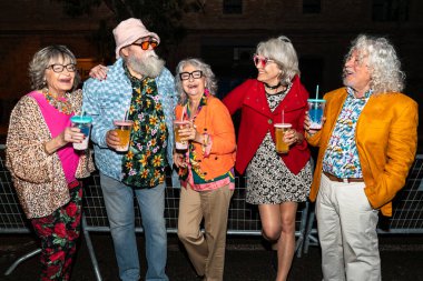 Süslü elbiseli mutlu son sınıf arkadaşları gecenin bir yarısı şehir sokaklarında parti veriyor. Şık kıyafetler giyen ve dışarıda eğlenen neşeli yaşlı insanlar.