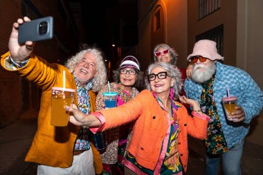 Süslü elbiseli mutlu son sınıf arkadaşları gecenin bir yarısı şehir sokaklarında parti veriyor. Şık kıyafetler giyen ve dışarıda eğlenen neşeli yaşlı insanlar.