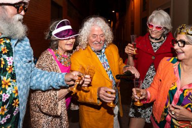 Süslü elbiseli mutlu son sınıf arkadaşları gecenin bir yarısı şehir sokaklarında parti veriyor. Şık kıyafetler giyen ve dışarıda eğlenen neşeli yaşlı insanlar.