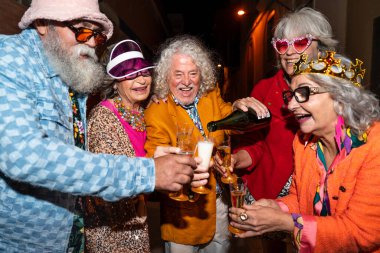 Süslü elbiseli mutlu son sınıf arkadaşları gecenin bir yarısı şehir sokaklarında parti veriyor. Şık kıyafetler giyen ve dışarıda eğlenen neşeli yaşlı insanlar.