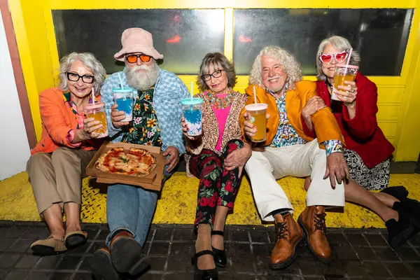 Süslü elbiseli mutlu son sınıf arkadaşları gecenin bir yarısı şehir sokaklarında parti veriyor. Şık kıyafetler giyen ve dışarıda eğlenen neşeli yaşlı insanlar.