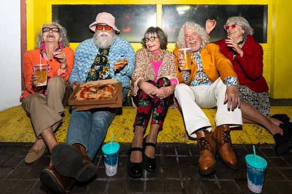 Süslü elbiseli mutlu son sınıf arkadaşları gecenin bir yarısı şehir sokaklarında parti veriyor. Şık kıyafetler giyen ve dışarıda eğlenen neşeli yaşlı insanlar.