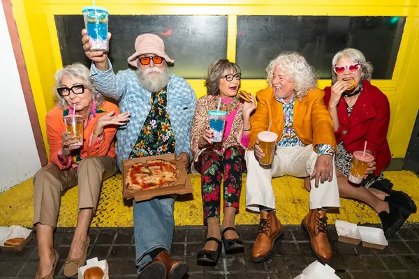 Süslü elbiseli mutlu son sınıf arkadaşları gecenin bir yarısı şehir sokaklarında parti veriyor. Şık kıyafetler giyen ve dışarıda eğlenen neşeli yaşlı insanlar.