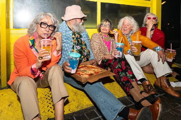 Süslü elbiseli mutlu son sınıf arkadaşları gecenin bir yarısı şehir sokaklarında parti veriyor. Şık kıyafetler giyen ve dışarıda eğlenen neşeli yaşlı insanlar.