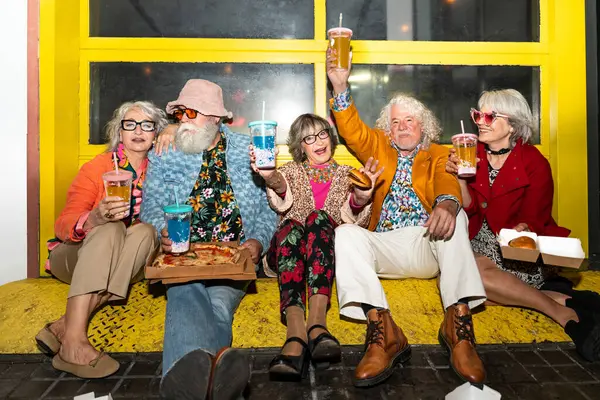 Süslü elbiseli mutlu son sınıf arkadaşları gecenin bir yarısı şehir sokaklarında parti veriyor. Şık kıyafetler giyen ve dışarıda eğlenen neşeli yaşlı insanlar.