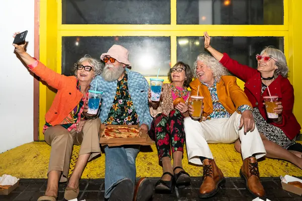 Süslü elbiseli mutlu son sınıf arkadaşları gecenin bir yarısı şehir sokaklarında parti veriyor. Şık kıyafetler giyen ve dışarıda eğlenen neşeli yaşlı insanlar.