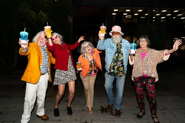 Süslü elbiseli mutlu son sınıf arkadaşları gecenin bir yarısı şehir sokaklarında parti veriyor. Şık kıyafetler giyen ve dışarıda eğlenen neşeli yaşlı insanlar.