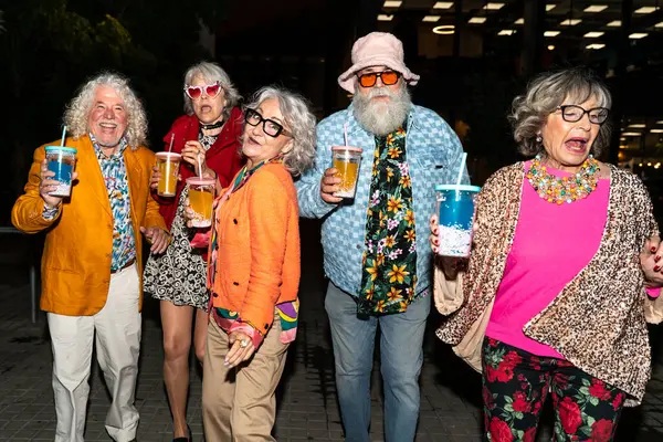 Süslü elbiseli mutlu son sınıf arkadaşları gecenin bir yarısı şehir sokaklarında parti veriyor. Şık kıyafetler giyen ve dışarıda eğlenen neşeli yaşlı insanlar.