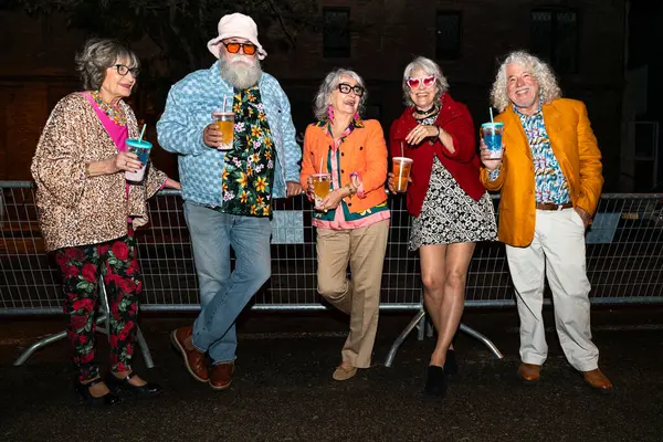 Süslü elbiseli mutlu son sınıf arkadaşları gecenin bir yarısı şehir sokaklarında parti veriyor. Şık kıyafetler giyen ve dışarıda eğlenen neşeli yaşlı insanlar.