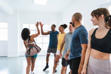 Spor salonunda egzersiz yapan çok ırklı bir grup sporcu, spor salonunda egzersiz yaptıktan sonra kişisel antrenörlerine beşlik çakıyor.