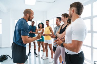 Çok ırklı spor yapan bir grup sporcu, eğitim sınıfındaki çeşitli sporcuların antrenmanlarında antrenman yaparken kişisel antrenörlerini dinliyorlar. Bir eğitim sırasında bir not panosuyla rehberlik ediyorlar. 