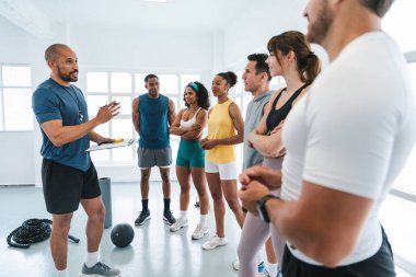 Çok ırklı spor yapan bir grup sporcu, beden eğitimi sınıfında spor yapıyor. Çok ırklı sporculardan oluşan bir grup, özel antrenörlerini dinliyorlar. Parlak bir spor salonunda spor yapıyorlar.
