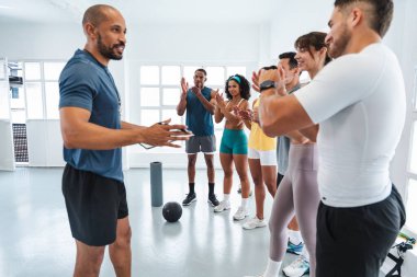 Çok ırklı spor yapan bir grup sporcu çeşitli spor salonlarında antrenman yapıyor. Çeşitli sporcular başarılı bir egzersiz sonrası antrenörlerini alkışlıyor ve tebrik ediyorlar.