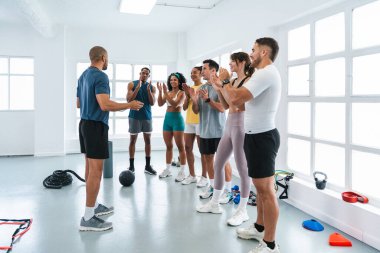 Çok ırklı spor yapan bir grup sporcu, çok yönlü spor salonlarında çeşitli sporcuları alkışlıyor. Parlak spor eğitimini tamamladıktan sonra kişisel antrenörlerini alkışlıyorlar.