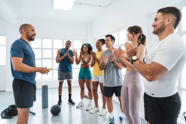Spor salonunda spor yapan çok ırklı bir grup sporcu, spor salonunda egzersiz yaptıktan sonra antrenörlerini alkışlıyor ve kişisel antrenörlerini kutluyorlar.
