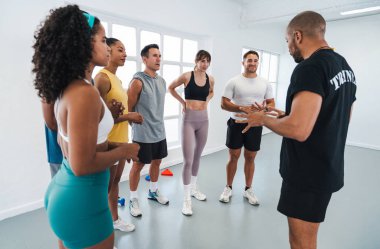 Çok ırklı spor yapan bir grup sporcu, spor salonunda spor yapıyor. Spor salonundaki sporculara işlevsel antrenmanları açıklıyorlar.