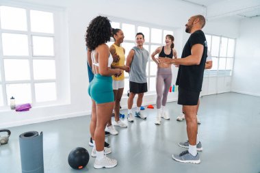 Çok ırklı spor yapan bir grup sporcu, spor salonunda spor yapıyor ve bir grup farklı sporcuya işlevsel bir antrenman yaptıklarını açıklıyorlar. Modern spor salonu