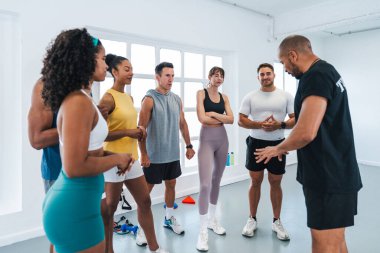 Çok ırklı bir grup sporcu, beden eğitimi sınıfında çeşitli sporcular çalıştırıyor. Modern spor salonundaki işlevsel eğitim sırasında dikkatle antrenörlerin rehberliğini dinliyorlar.