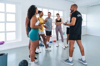 Çok ırklı spor yapan bir grup sporcu, modern bir spor salonundaki çeşitli sporculara beden eğitimi eğitimi çalıştırıyor.