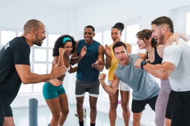 Çok ırklı spor yapan bir grup sporcu beden eğitimi sınıfında çok ırklı sporcular ve onların antrenörleri parlak bir spor salonunda yaptıkları egzersiz sırasında başarıyı kutluyorlar.