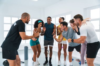 Çok ırklı spor yapan bir grup sporcu, sportif bir antrenmanı tamamladıktan sonra beden eğitimi sınıfındaki çeşitli sporcuların antrenmanlarını fitness koçlarıyla kutluyorlar. Motivasyon