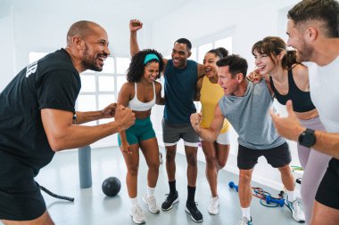 Antrenman sınıfında spor yapan çok ırklı sporcu grubu antrenörleriyle fitness başarılarını kutluyor.
