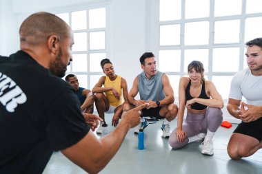 Spor salonunda spor yapan çok ırklı bir grup sporcu spor salonunda spor salonunda bir çemberin içinde oturuyorlar.