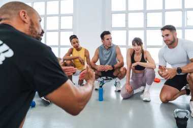Spor salonunda spor yapan çok ırklı bir grup sporcu beden eğitimi sınıfında spor salonunda oturuyorlar.