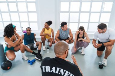 Antrenörlerini dinleyen bir grup genç sporcu, parlak bir spor salonunda yeni işlevsel egzersizleri anlatıyor.