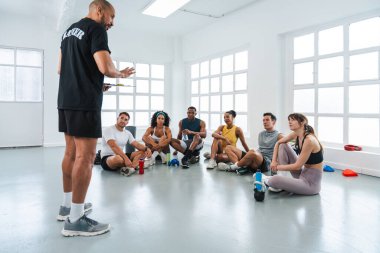 Spor salonunda spor yapan çok ırklı bir grup sporcu spor salonunda çok ırklı bir grup sporcu bir spor salonunda oturup antrenörlerinin yaptığı bir egzersizi dinliyorlar.