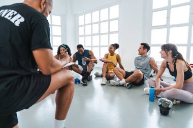 Çok ırklı spor yapan bir grup sporcu, beden eğitimi sınıfında spor yapıyor. Çok ırklı sporcular antrenörleriyle tartışıyor.