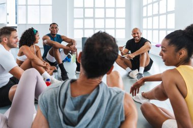 Çok ırklı spor yapan bir grup sporcu, çok ırklı sporculardan oluşan bir spor salonunda egzersiz yapıyor. İşlevsel bir eğitim seansından sonra antrenörleriyle sohbet ediyorlar. 