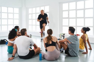 Spor salonunda spor yapan çok ırklı bir grup sporcu spor salonunda çok ırklı sporcular spor salonunun zemininde oturmuş, eğitmenlerinin bir eğitim egzersizini göstermelerini izliyorlar.