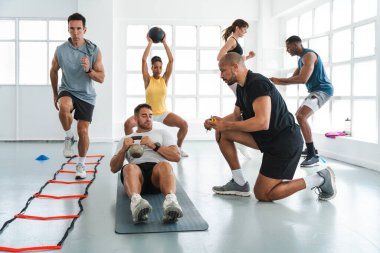 Çok ırklı spor yapan bir grup sporcu, beden eğitimi sınıfında çok ırklı erkek ve kadın sporculardan oluşan bir spor salonunda spor salonunda kişisel antrenörle antrenman yapıyor.