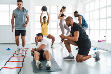 Çok ırklı spor yapan bir grup sporcu, beden eğitimi sınıfında çeşitli sporcuların parlak bir spor hocasıyla antrenman yapıyor. Modern spor salonu