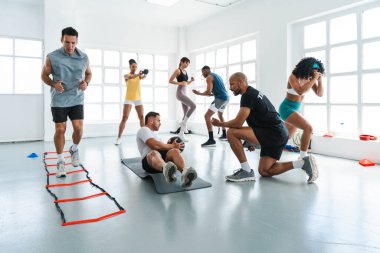 Çok ırklı spor yapan bir grup sporcu, parlak, modern bir spor salonunda, bir spor salonunda, bir fitness koçunu takip eden çeşitli bireylerden oluşan bir eğitim sınıfında egzersiz yapıyorlar.