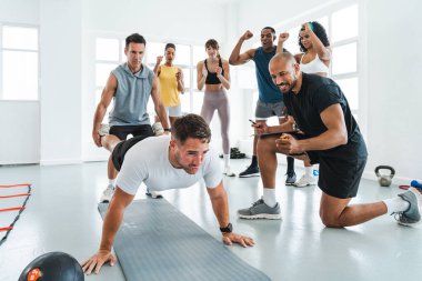 Antrenman sınıfında spor yapan çok ırklı bir grup sporcu sporcu, sporcuları kişisel antrenörlerinin rehberliğinde yüksek şınav çeken bir sporcuya tezahürat yapmaya motive etti. 