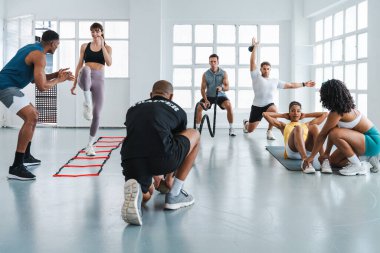 Çok ırklı spor yapan bir grup sporcu, beden eğitimi sınıfında antrenörlük yapıyor. Çeşitli sporculara çeşitli fitnelerle dolu parlak bir spor salonunda işlevsel eğitimlerini sürdürüyorlar.