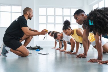 Çok ırklı spor yapan bir grup sporcu, beden eğitimi sınıfında çeşitli sporcuların antrenmanlarına katılıyor ve bir yandan kişisel antrenör tarafından, bir yandan da özel antrenör tarafından,