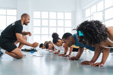 Çok ırklı bir grup sporcu beden eğitimi sınıfında egzersiz yapıyor. Çeşitli sporcular işlevsel bir antrenman sırasında parlak bir spor salonunda şınav çekiyorlar.