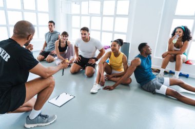 Çok ırklı spor yapan bir grup sporcu, antrenörlerini dinleyen çok ırklı sporculardan oluşan bir spor salonunda egzersiz yapıyorlar.