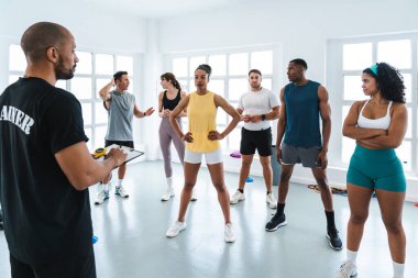 Çok ırklı spor yapan bir grup sporcu, parlak bir spor salonunda antrenman yaparken antrenörlerini dinleyen farklı sporcularla antrenman yapıyor.