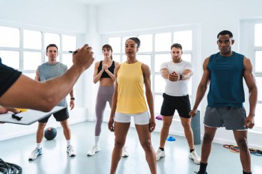 Çok ırklı bir grup sporcu, işlevsel antrenman yapıyor. Spor sınıfındaki çeşitli sporcular, özel antrenörlerinin rehberliğinde, işlevsel bir eğitim sırasında spor salonunda egzersiz yapıyorlar.