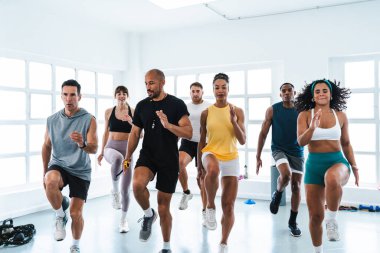 Çok ırklı spor yapan bir grup sporcu, spor sınıfında çeşitli sporcuların eğitimleri sırasında spor yaparken yüksek diz egzersizi yapıyorlar.